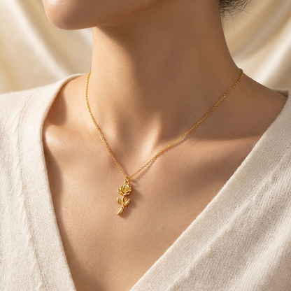 Gold necklace with a rose pendant worn by a person in a white outfit.